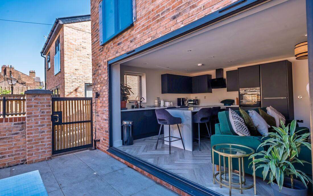 Bi-fold doors opening from a brick house onto a paved terrace.