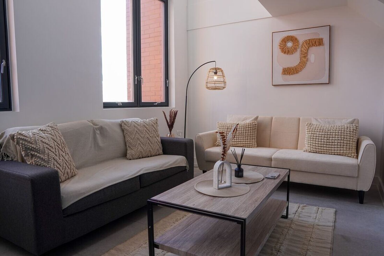 The living room of a managed short-let apartment, with tall windows and a red-brick building opposite.